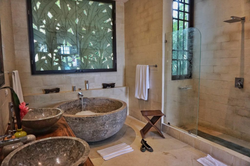 This beautiful bathroom features natural tiles, carved stone, a granite tub, and his and hers sinks.