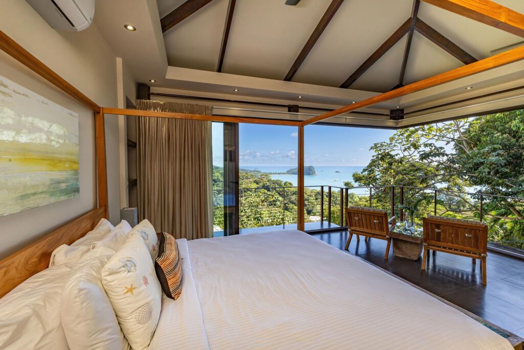 Soft light fills this serene bedroom as sliding doors open to jungle and ocean views, creating a quiet, open retreat designed for rest, reflection, and unhurried mornings.