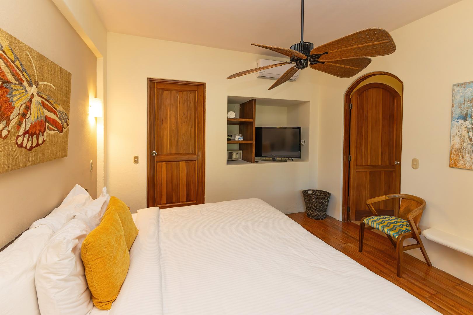 Bedroom with king bed, wooden doors, ceiling fan, wall-mounted television, and warm accent pillows