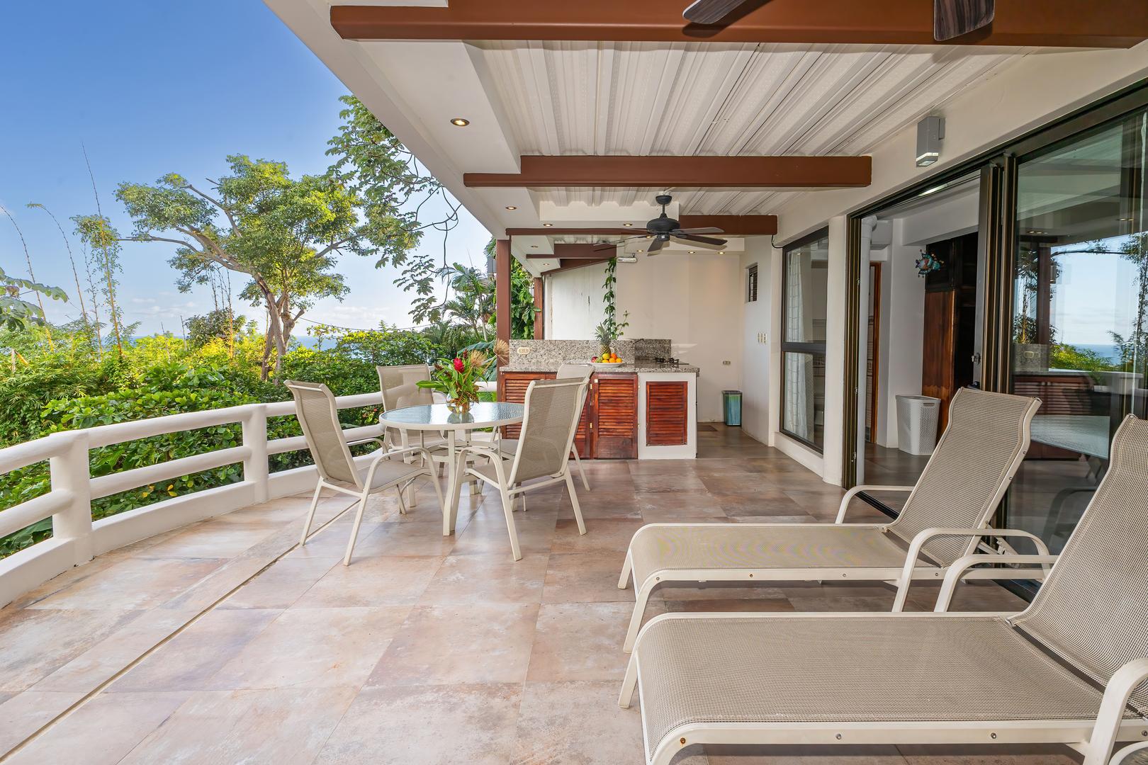 Covered terrace accessed from a twin bedroom with outdoor kitchen, dining table, loungers, and tropical surroundings
