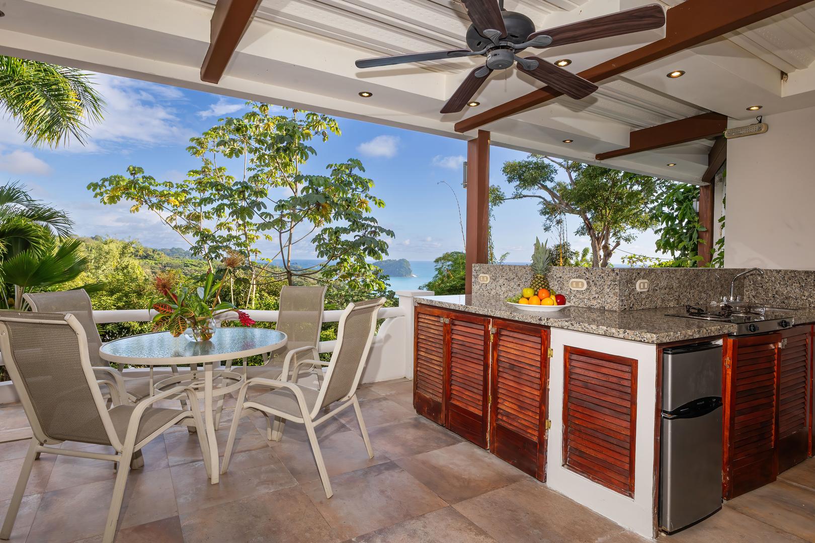 Covered terrace accessed from a twin bedroom with outdoor kitchen, dining table, ocean view, and tropical trees