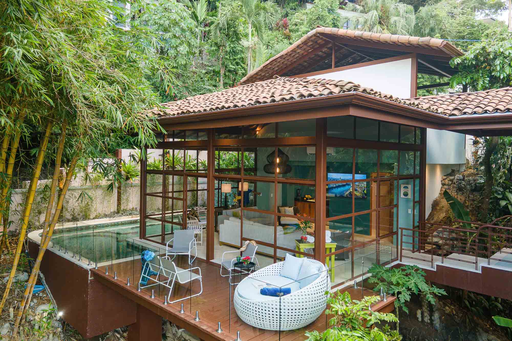 Exterior view of the new glass-walled wing with wooden deck, outdoor seating, and jungle surroundings at a luxury villa in Manuel Antonio, Costa Rica.