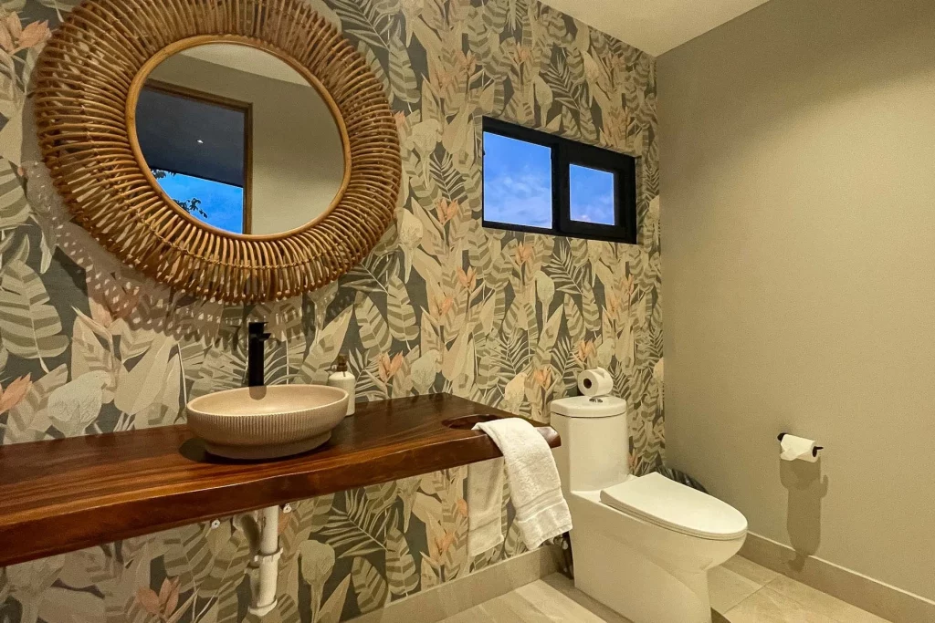The tropical-themed walls of this bathroom fit well with the native wood and natural mirror.