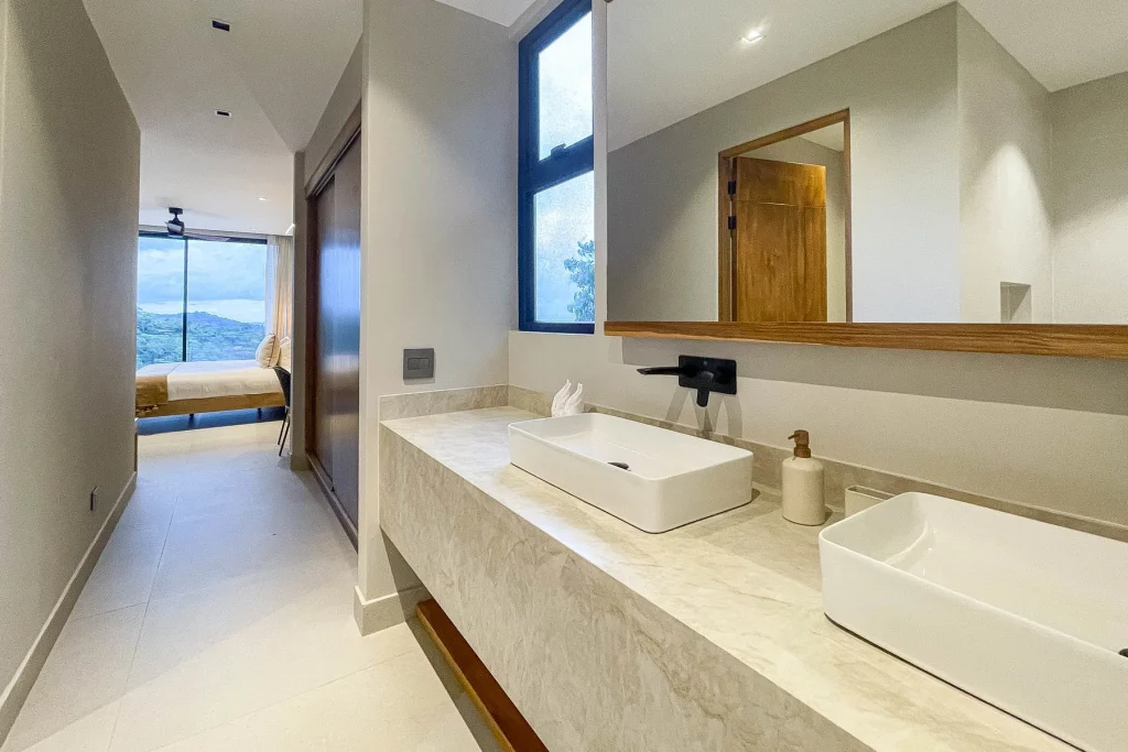 
This contemporary ensuite bathroom features a spacious closet and twin sinks atop a stunning stone countertop.